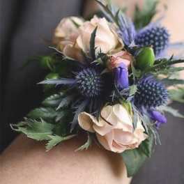 Small wrist corsage with pale roses and blue thistle-like flowers