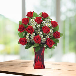 Red roses and white daisy-like flowers in a red glass vase