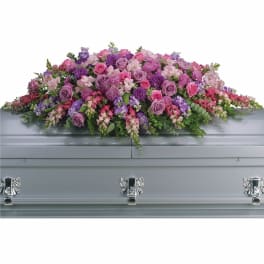 Pink and purple casket spray of roses, snapdragons, and mixed blooms on a gray casket