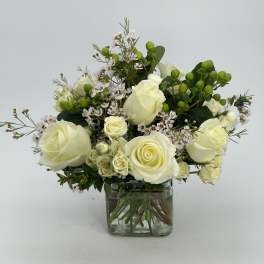 Arrangement of cream roses and small pink blossoms with green berries in a clear glass cube vase