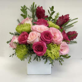Pink and fuchsia roses with green mums and red accents arranged in a white cube vase.