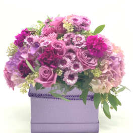 Lavender and pink roses, carnations, mums, and hydrangeas arranged in a lavender box container