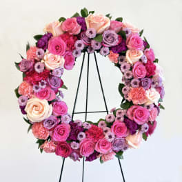 Round floral wreath of pink, peach, and purple roses on a black stand