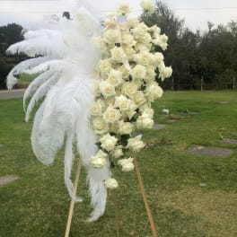 Tall white rose standing spray with large white feathers on an easel