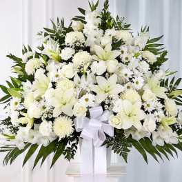 Large white funeral spray with lilies, roses, and daisies on a stand