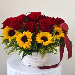 Red roses and yellow sunflowers in a white basket with a burgundy ribbon