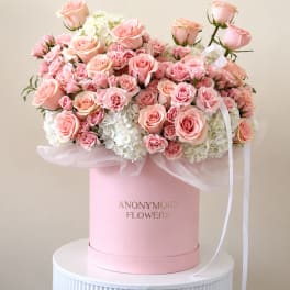 Pink roses and white hydrangeas arranged in a pink hat box with ribbon.