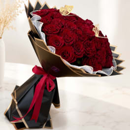 Bouquet of red roses wrapped in black and gold paper with a red ribbon