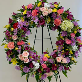 Heart-shaped floral wreath with pink, purple, yellow, and white blooms on a black stand