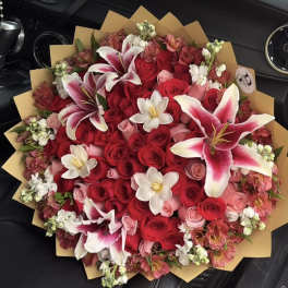 Large bouquet of red and pink roses with white lilies in brown wrap
