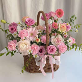 Pink and white flower arrangement in a wicker basket with ribbon