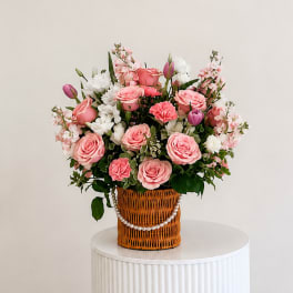Pink and white flower arrangement in a wicker basket with a pearl garland
