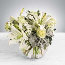 Low arrangement of white lilies, roses, and stock in a round clear glass vase