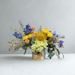 Colorful bouquet in a white floral vase with yellow, blue, pink, and green blooms