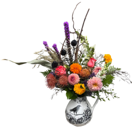 Mixed bouquet in a decorative white pitcher vase with pink, orange, and purple flowers