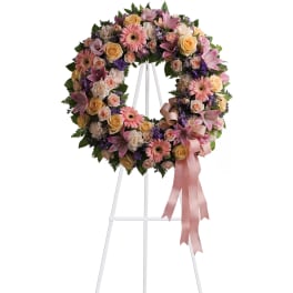 Standing wreath of pink lilies, roses, gerberas, and mixed pastels on a white easel with ribbon bow