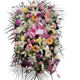 Large standing floral spray with pink, white, and purple blooms and a pink ribbon
