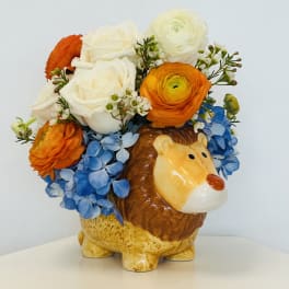 Flower arrangement in a ceramic lion planter with blue hydrangeas and orange and white blooms