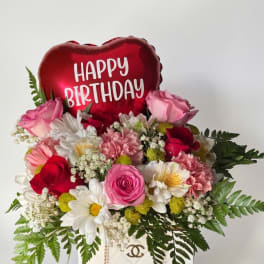 Pink and red flower arrangement with a heart-shaped Happy Birthday balloon in a white bag
