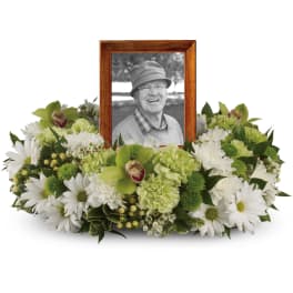 Low green and white sympathy wreath encircling a wooden frame with a black-and-white portrait