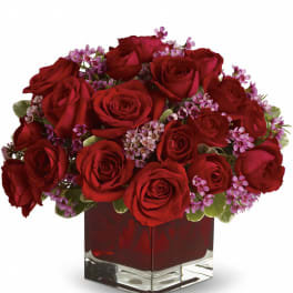 Low arrangement of red roses with small pink blooms in a square clear glass vase