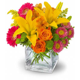 Bright mixed flower arrangement with yellow lilies and orange roses in a clear cube vase