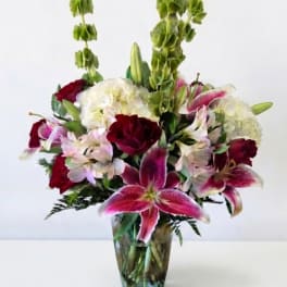 Mixed bouquet of lilies, hydrangeas, and red blooms in a glass vase
