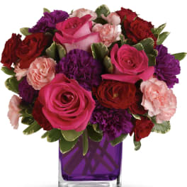 Compact bouquet of pink roses and red and purple carnations in a purple glass cube vase