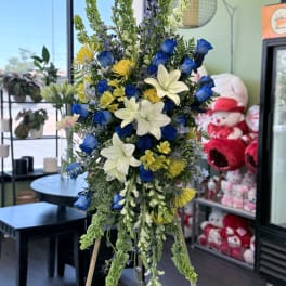 Tall standing floral spray with blue roses, white lilies, and yellow accents