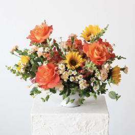 Bright mixed bouquet with orange roses and sunflowers in a white vase