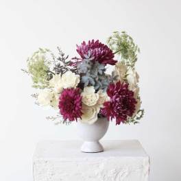Magenta and white flowers arranged in a white pedestal vase