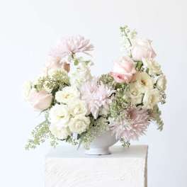 Soft pink and white floral arrangement in a white pedestal vase