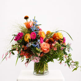 Colorful mixed bouquet in a clear glass vase with orange, pink, yellow, and blue flowers