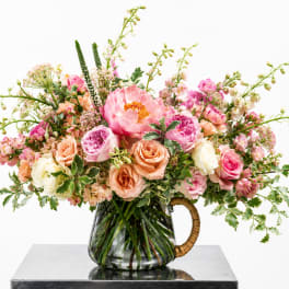 Pink and peach mixed flower arrangement in a glass pitcher vase