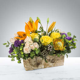 Mixed bouquet in a birch bark container with orange lilies, yellow roses, and purple blooms