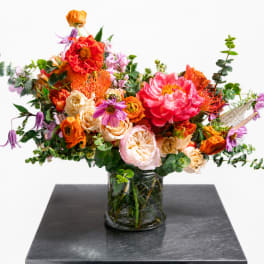 Mixed bouquet of orange, pink, and purple flowers in a glass vase