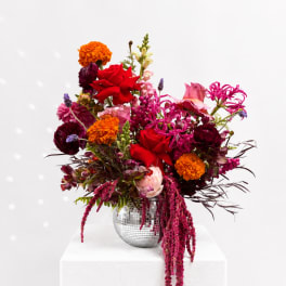 Bright mixed bouquet in a mirrored vase with red, pink, and orange blooms