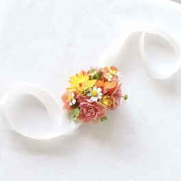 Small floral wrist corsage with pink, yellow, and orange blooms on a white ribbon