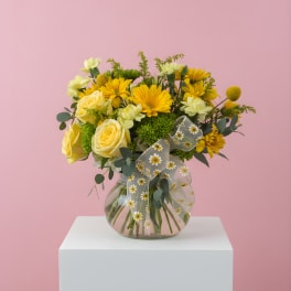 Yellow flowers in a clear glass vase with a sheer daisy ribbon
