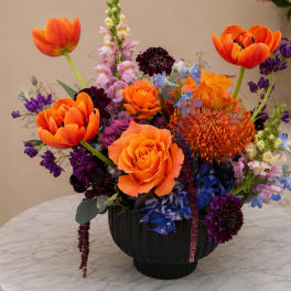 Bright mixed bouquet in a black vase with orange, purple, and blue flowers