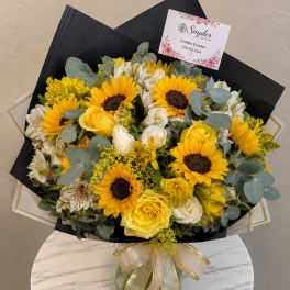 Bouquet of yellow sunflowers, yellow and white roses, and white alstroemeria in a glass vase