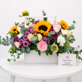 Mixed bouquet in a white wooden box with sunflowers, roses, and purple blooms