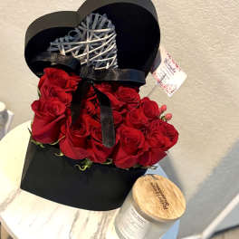 Red roses arranged in a black heart-shaped box with a ribbon and wicker heart topper
