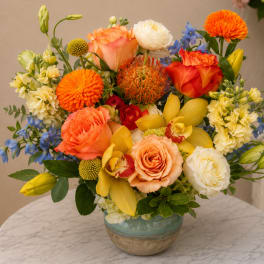 Mixed bouquet of orange, yellow, white, and blue flowers in a ceramic vase