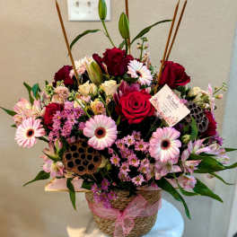 Mixed pink and red flower arrangement in a woven basket with a ribbon