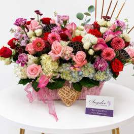 Pink and red mixed flower arrangement in a pink basket with ribbon