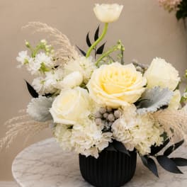 Cream roses and white flowers in a black vase with dried grasses