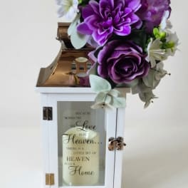 Purple and white floral arrangement on a white lantern with a candle inside