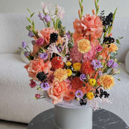 Mixed bouquet of peach, pink, purple, and yellow flowers in a white hat box