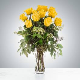 Yellow roses arranged in a clear glass vase with mixed greenery